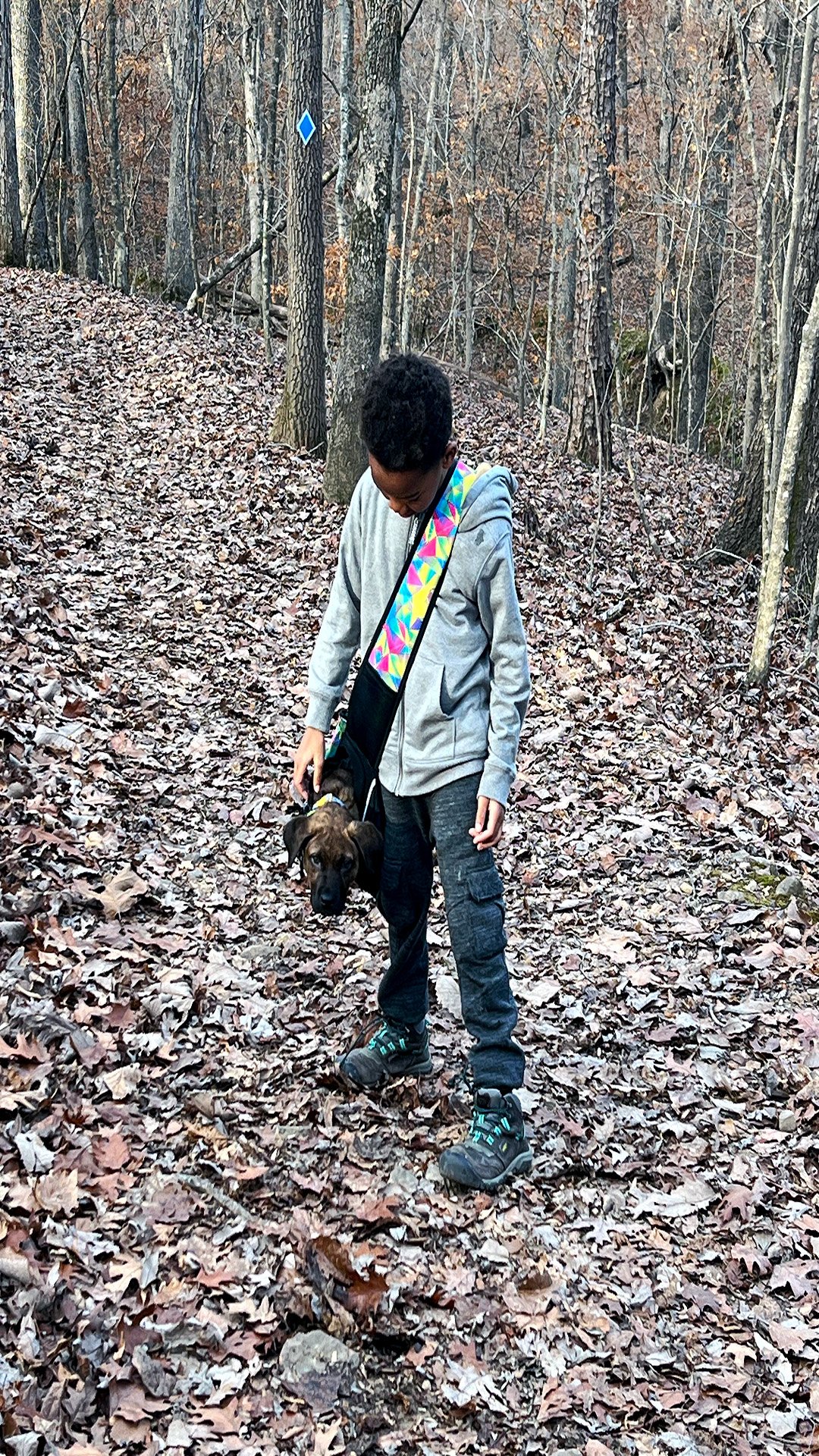 JJ carrying Gabe in a colorful carrier sling bag on the trail